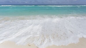 A beach with clear turquoise water and white foam waves.