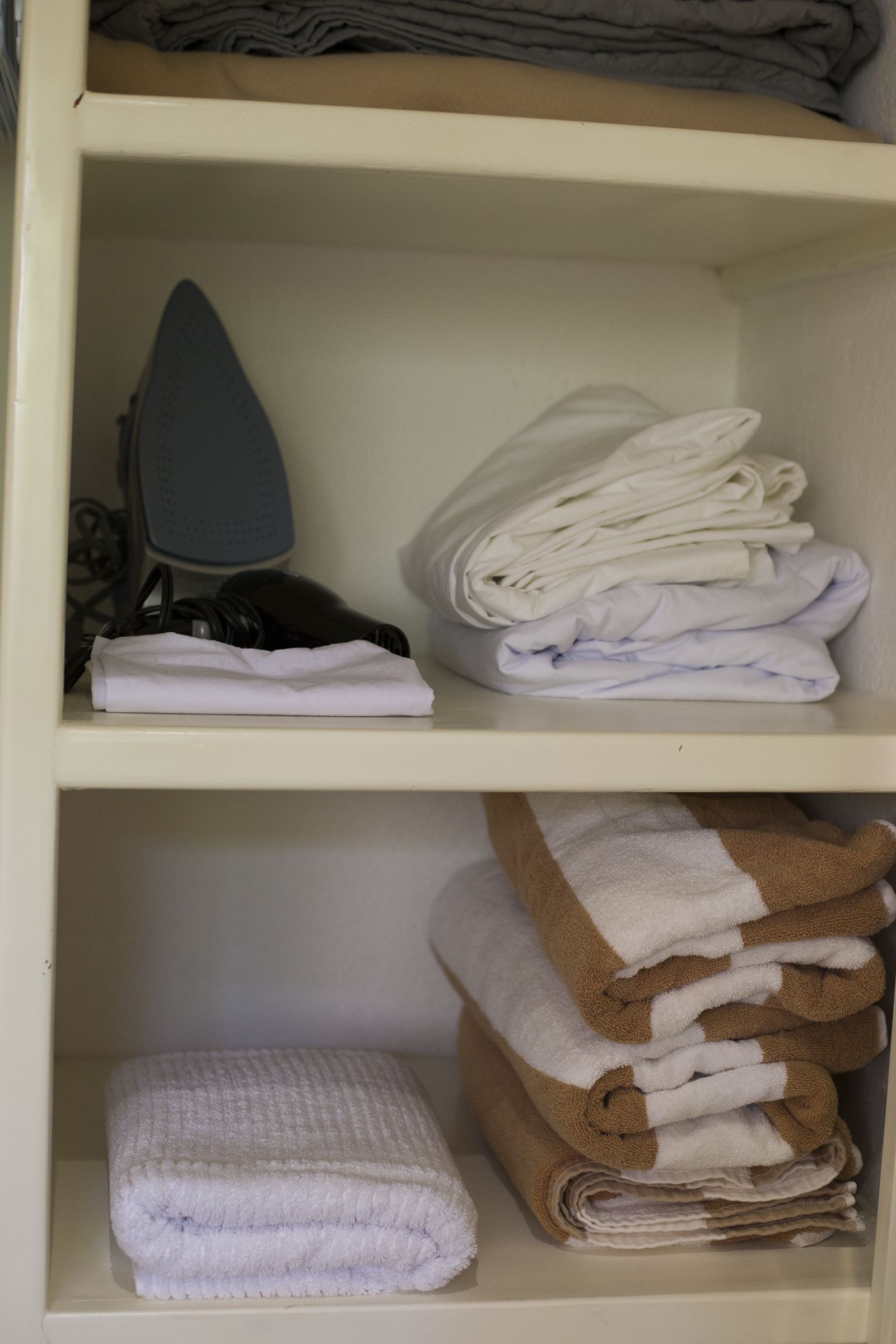 A storage unit with folded towels and an iron.