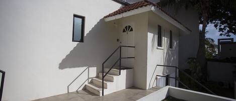 A white building with a tiled roof, a staircase with metal railings, and a small garden area with artificial grass.