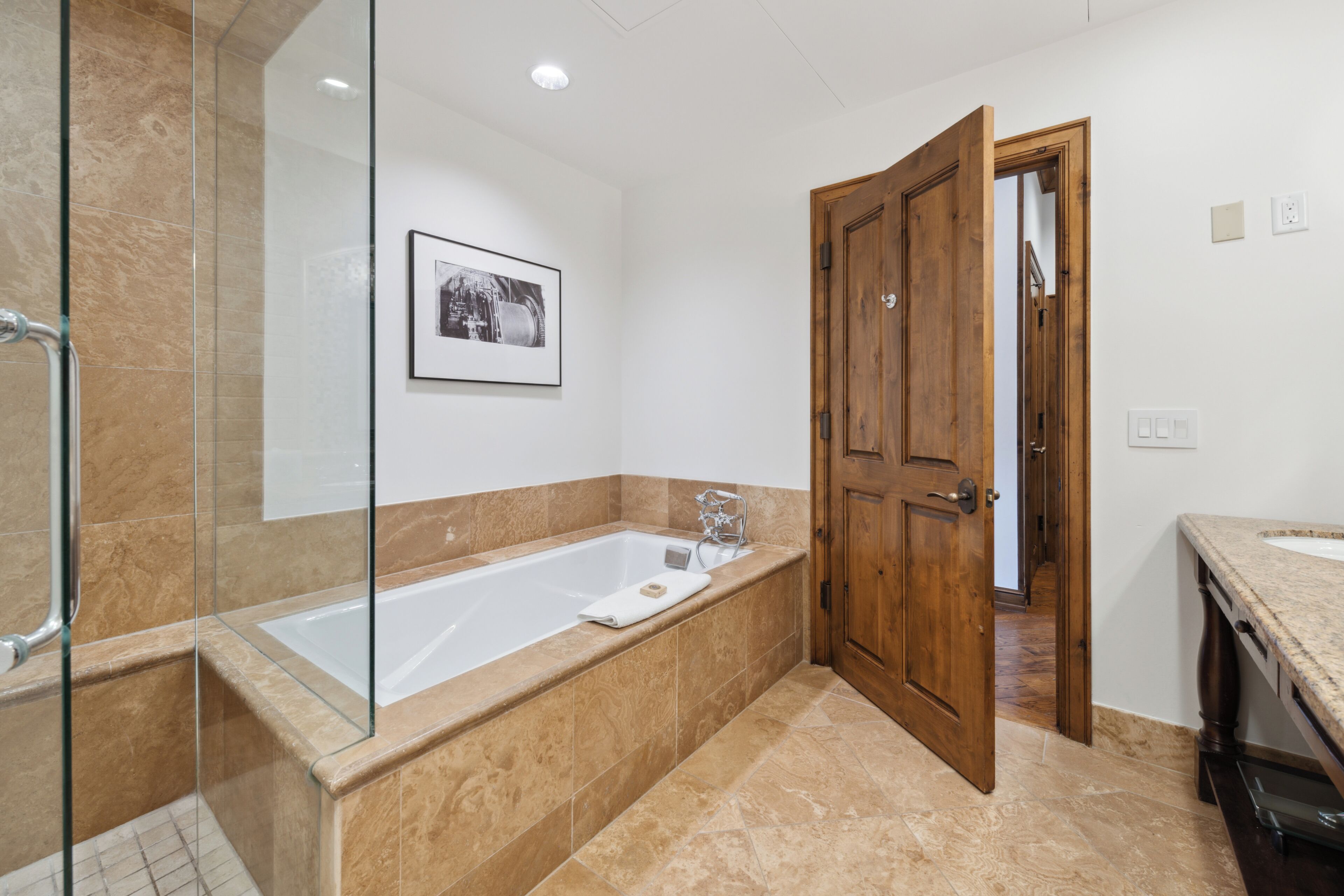 Une salle de bain moderne avec une douche à parois de verre, une grande baignoire et une porte en bois.