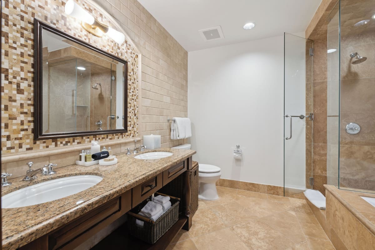 A modern bathroom with two sinks, a large mirror, a toilet, and a glass-enclosed shower.