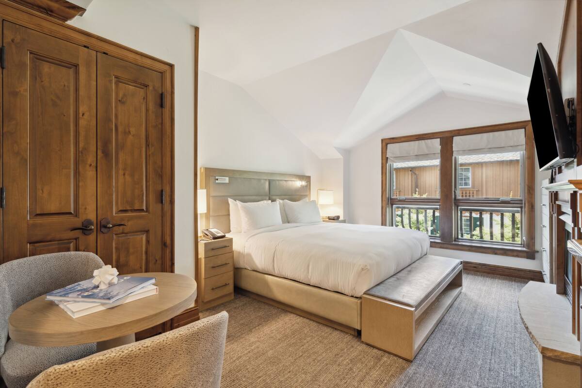 A bedroom with a bed, a desk with a chair, a wardrobe, and a television.