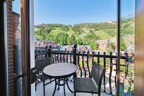 A balcony with a round table and chairs, offering a view of a green valley and buildings. - The Aspen Mountain Residences (Aspen)