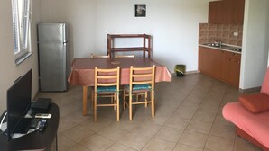 Un espace de vie compact comprenant une table à manger, deux chaises, un canapé, un coin cuisine et un réfrigérateur.