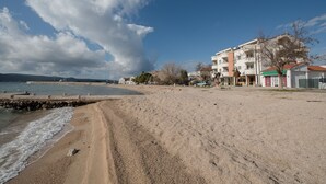 Une plage avec un rivage sablonneux, une digue rocheuse et des bâtiments en arrière-plan.