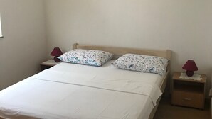 Un lit simple avec un cadre en bois, deux oreillers à motifs floraux et deux tables de chevet avec des lampes.