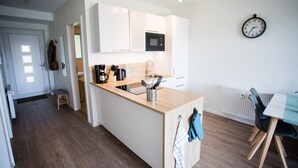 Een moderne keuken met een centraal eiland, witte kasten, een magnetron en een klok aan de muur.