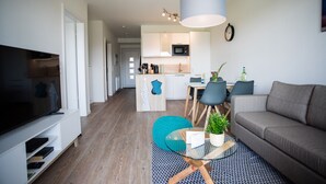 Een moderne woonkamer met een flatscreen televisie, een bank, een glazen salontafel en een eethoek met stoelen en een tafel.