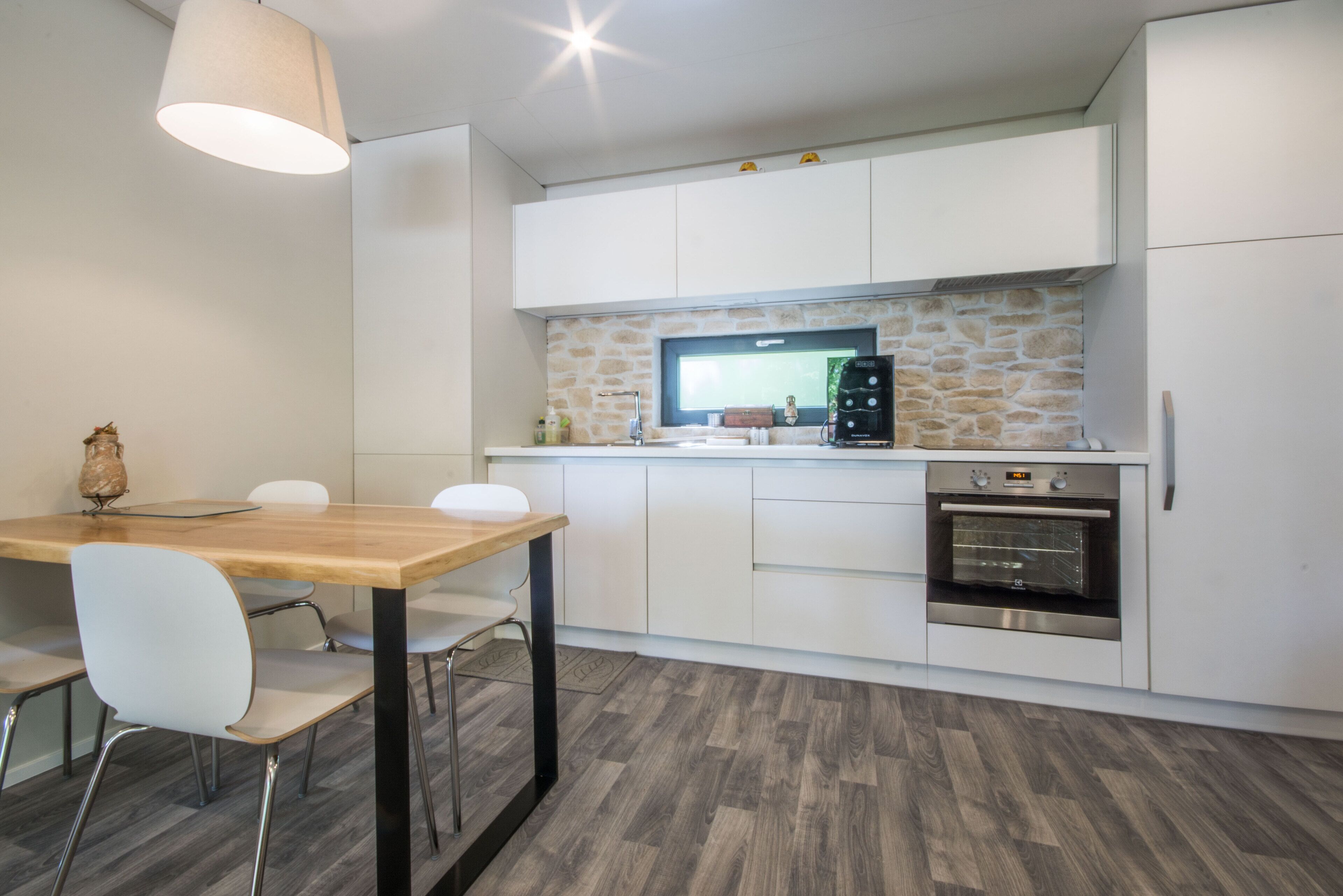 A modern kitchen with white cabinets, a built-in oven, and a stone backsplash.