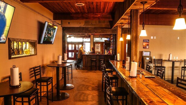 Un espace bar avec des tables et des chaises en bois, un comptoir avec une caisse enregistreuse et un téléviseur fixé au mur.