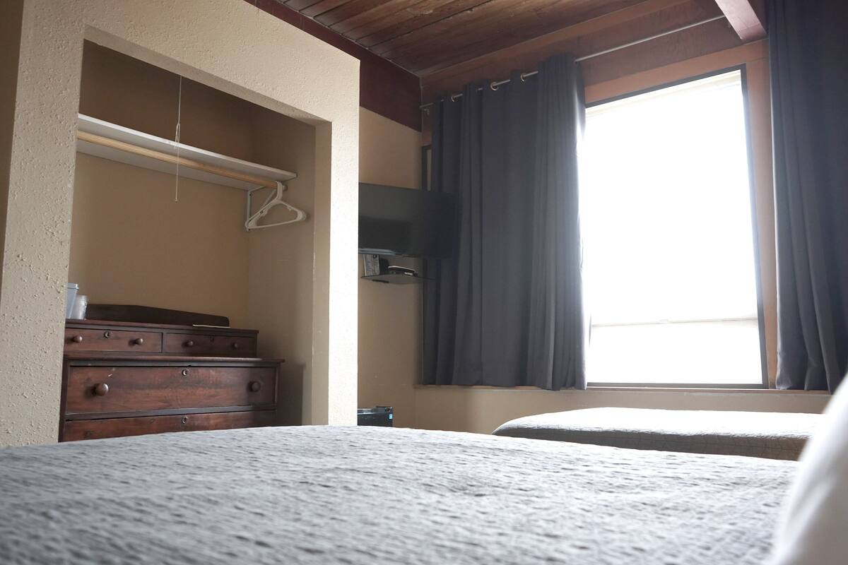 Une chambre à coucher avec un lit, une commode, un téléviseur et une fenêtre avec des rideaux.