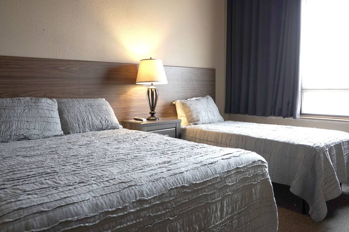 Une chambre d’hôtel avec deux lits, une table de chevet, une lampe et une fenêtre avec des rideaux.