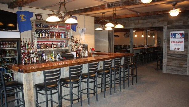 A bar area with a wooden counter, multiple bar stools, and a variety of liquor bottles. There are hanging lights and a sign indicating a teachers' lounge.