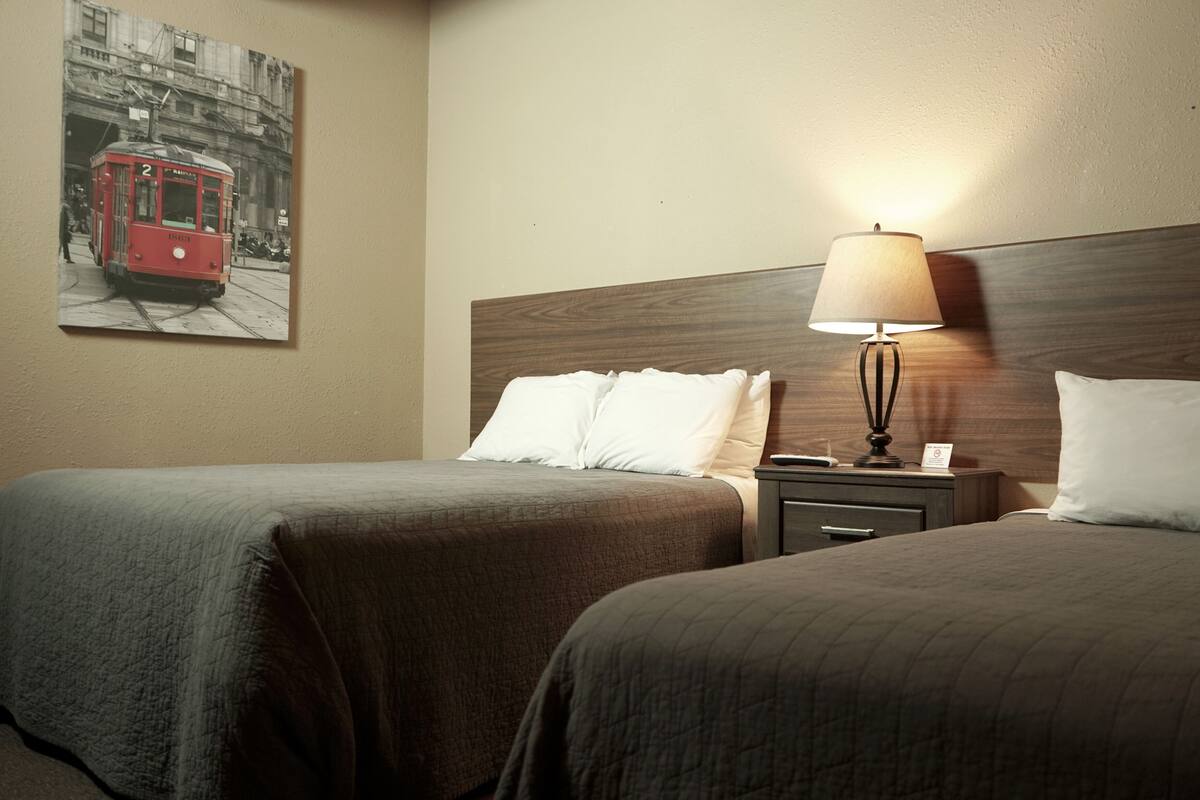Une chambre d’hôtel avec deux lits, une table de chevet, une lampe et un tableau représentant un tramway, accroché au mur.