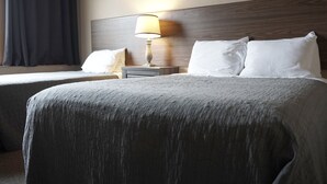 Une chambre d’hôtel avec deux lits, une table de chevet avec une lampe et une tête de lit.