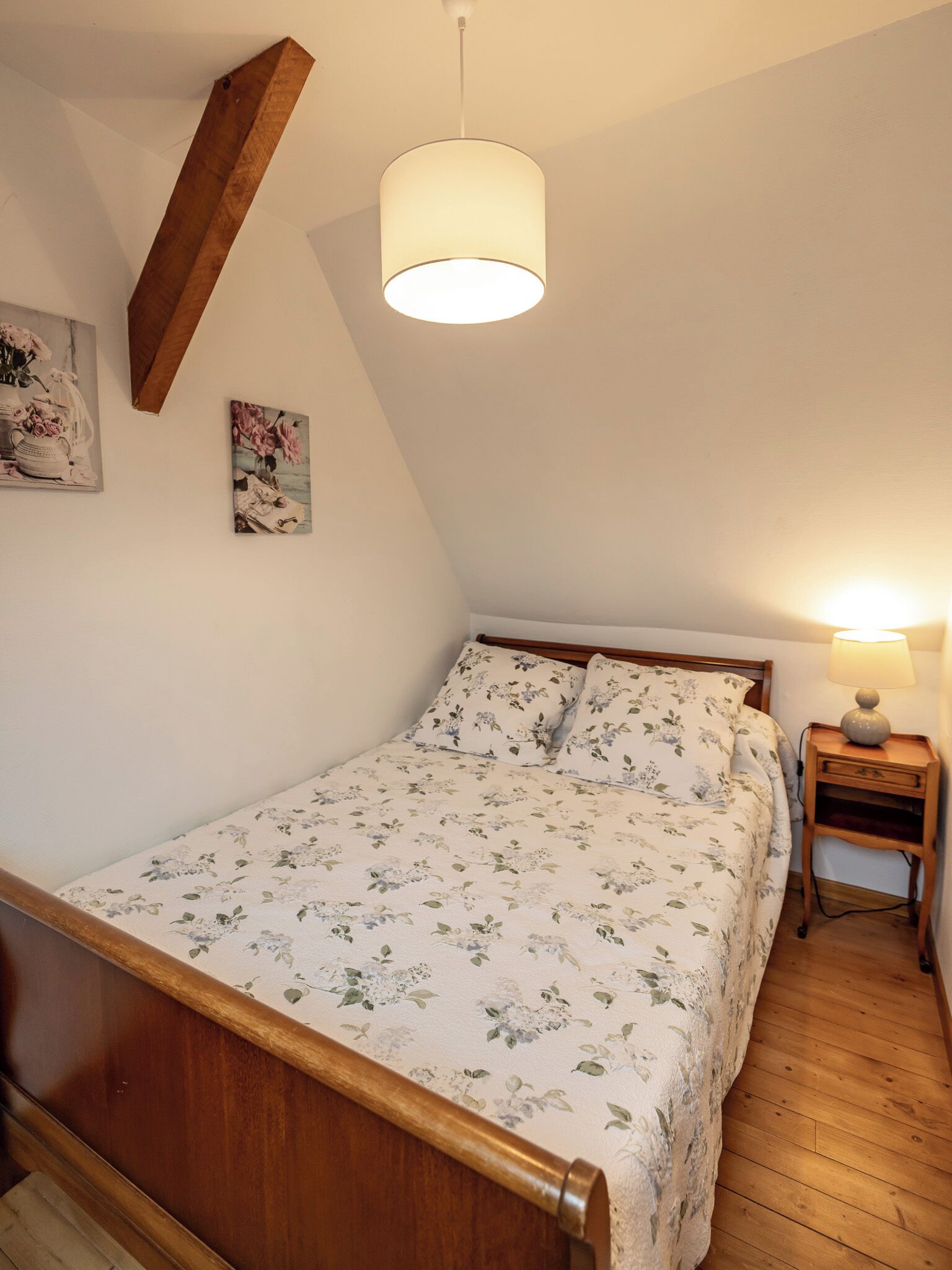 Une chambre à coucher avec un cadre de lit en bois, un luminaire suspendu, une table de chevet avec une lampe et une literie à motifs floraux.