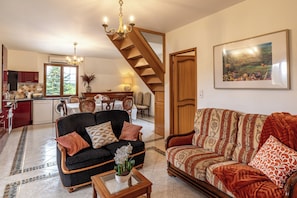 A spacious living area with a staircase, a dining table, and a kitchen in the background.
