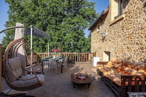 A patio with a hanging chair, a table with chairs, a sofa, and a stone wall.