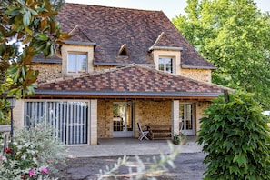 A two-story stone house with a sloped roof, a covered porch, and a gravel driveway.
