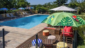 Piscina com espreguiçadeiras e guarda-sóis, rodeada por vegetação.