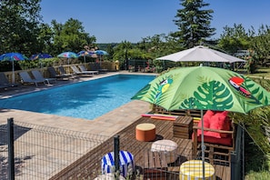 A swimming pool with lounge chairs and umbrellas, surrounded by greenery.