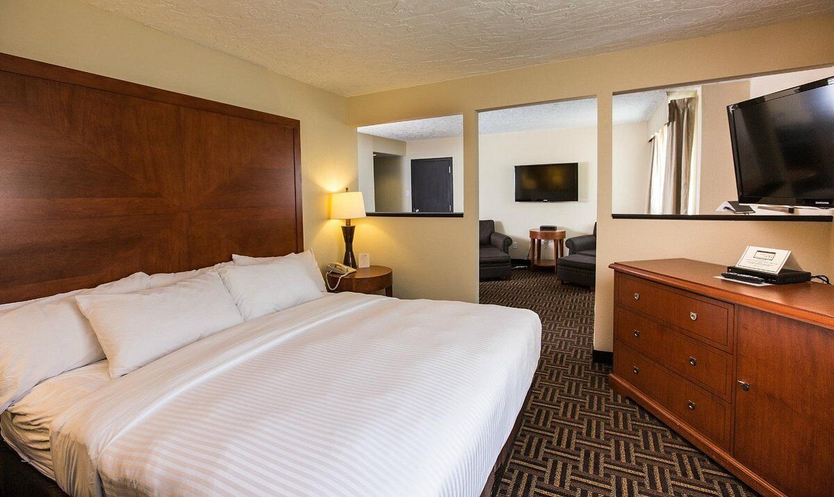 A hotel room with a large bed, a wooden headboard, a desk with a lamp, a television, and a mirror.