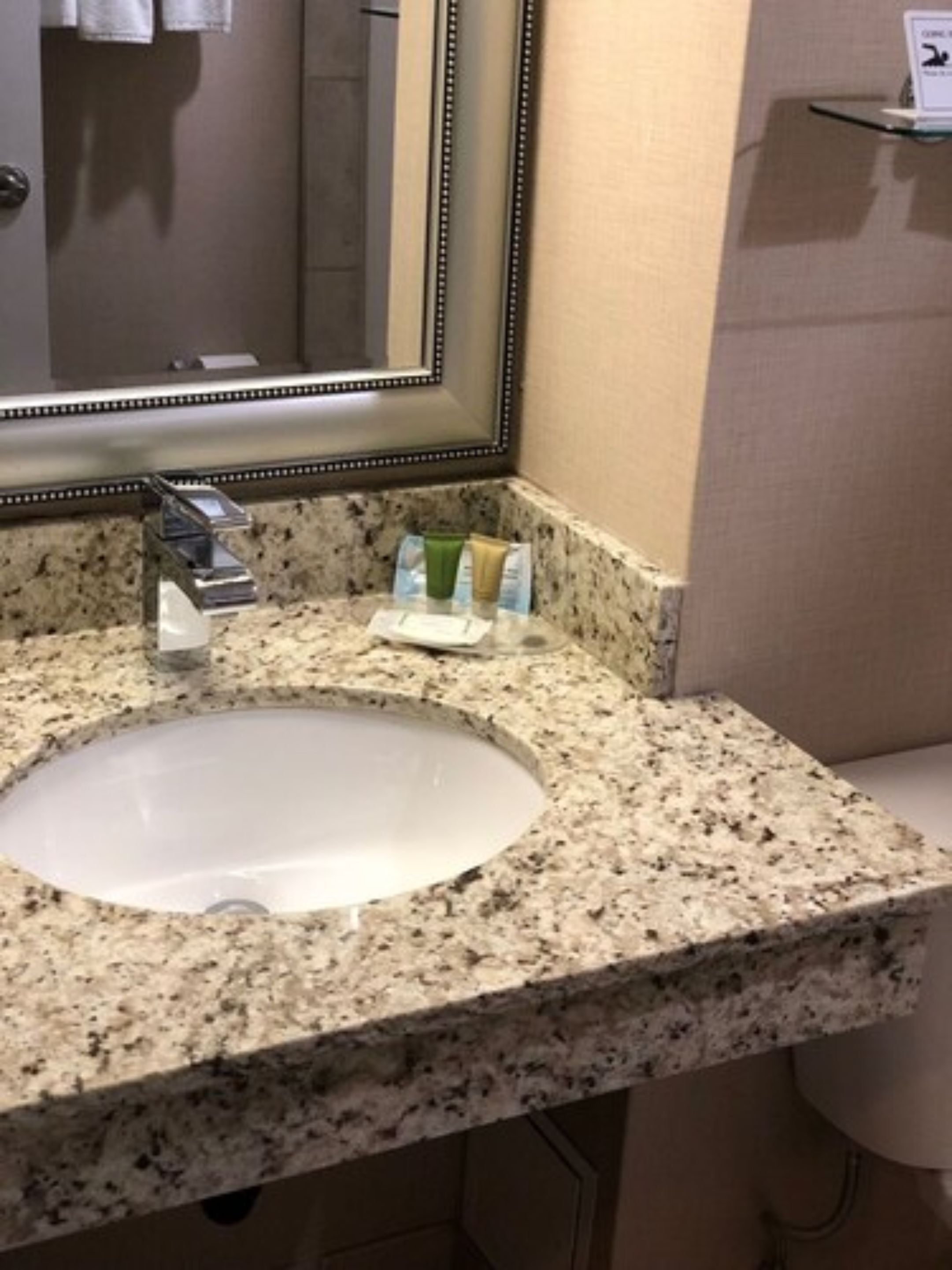 A bathroom with a granite countertop, a white sink, a mirror, and toiletries on the counter.