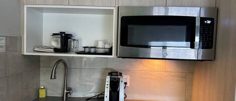 A compact kitchen with a stainless steel microwave, a coffee maker, and a sink.