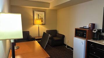 Une chambre d’hôtel compacte comprenant un bureau en bois, une chaise, un petit réfrigérateur, un four à micro-ondes, une machine à café et un tableau encadré au mur.