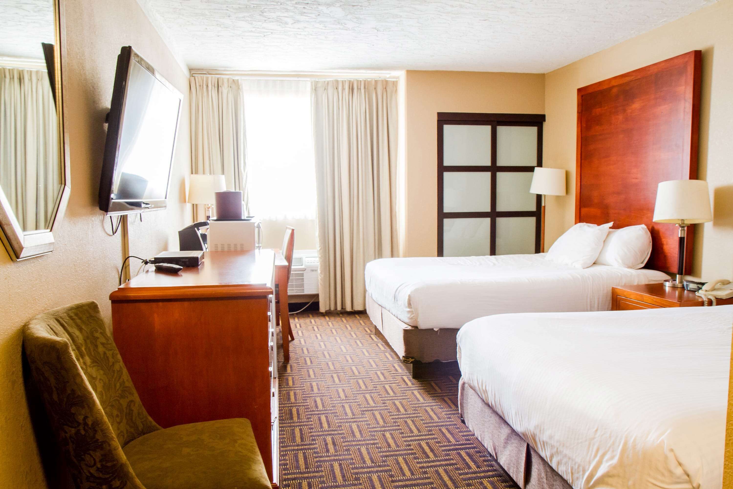 A hotel room with two beds, a desk, a chair, a TV, and a window with curtains.