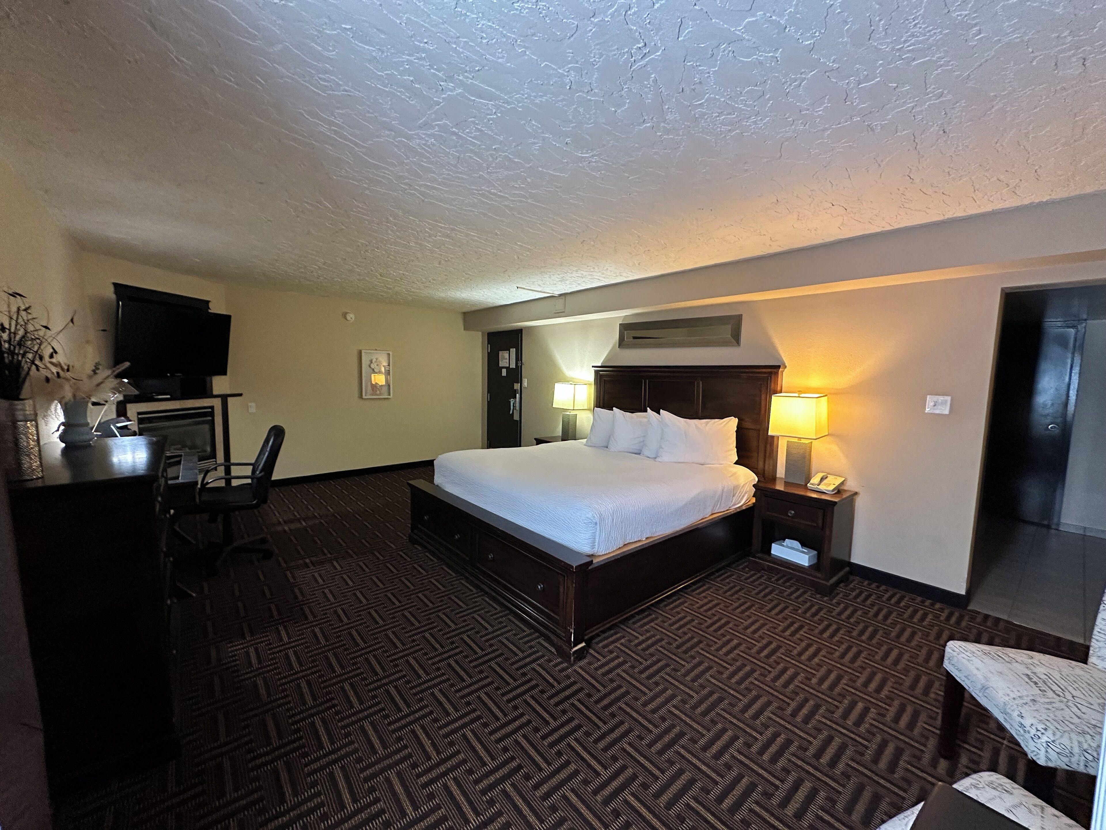 A hotel room with a large bed, a desk with a chair, a television, and a door.