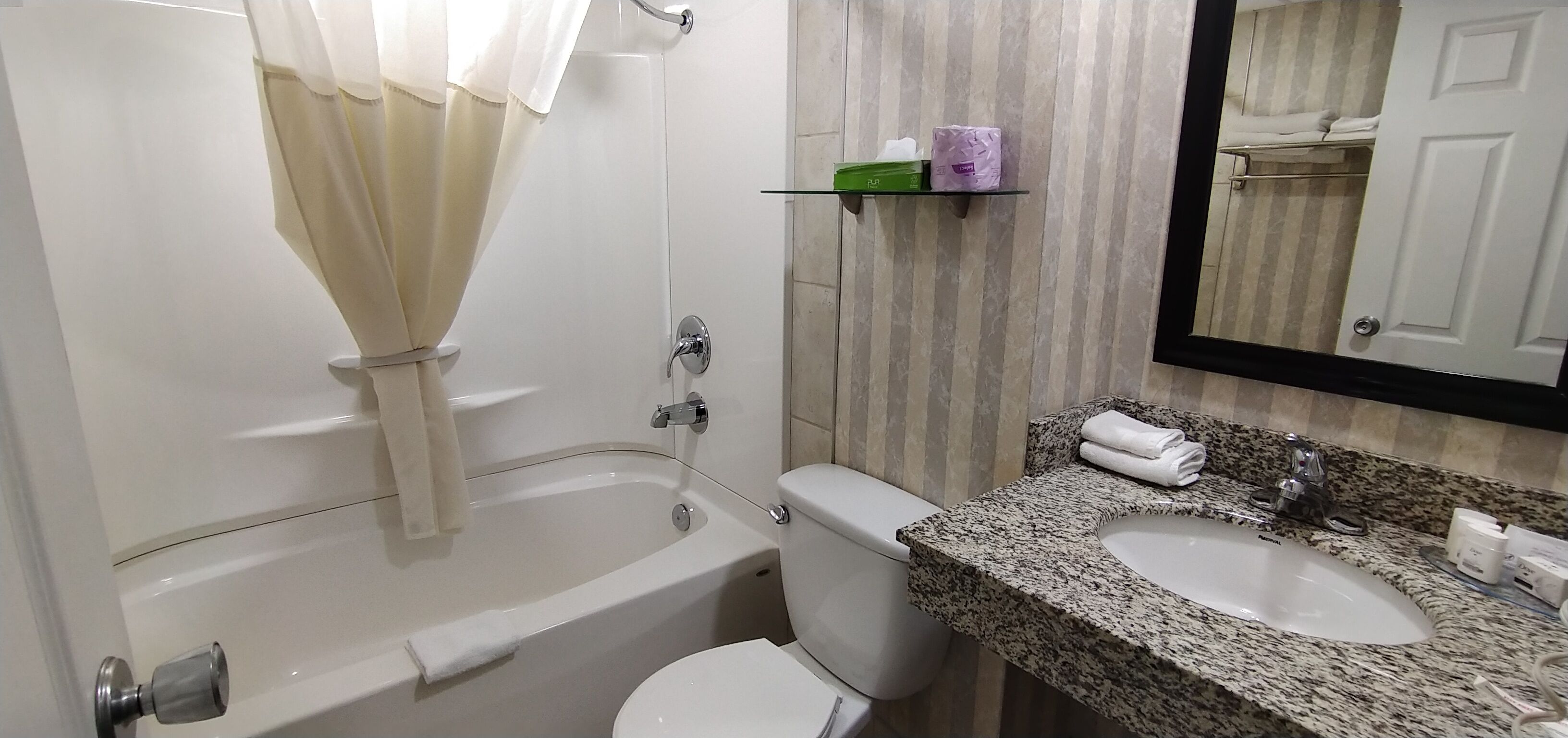 A bathroom with a bathtub, toilet, and two sinks. There is a mirror above the sinks and a towel rack on the wall.