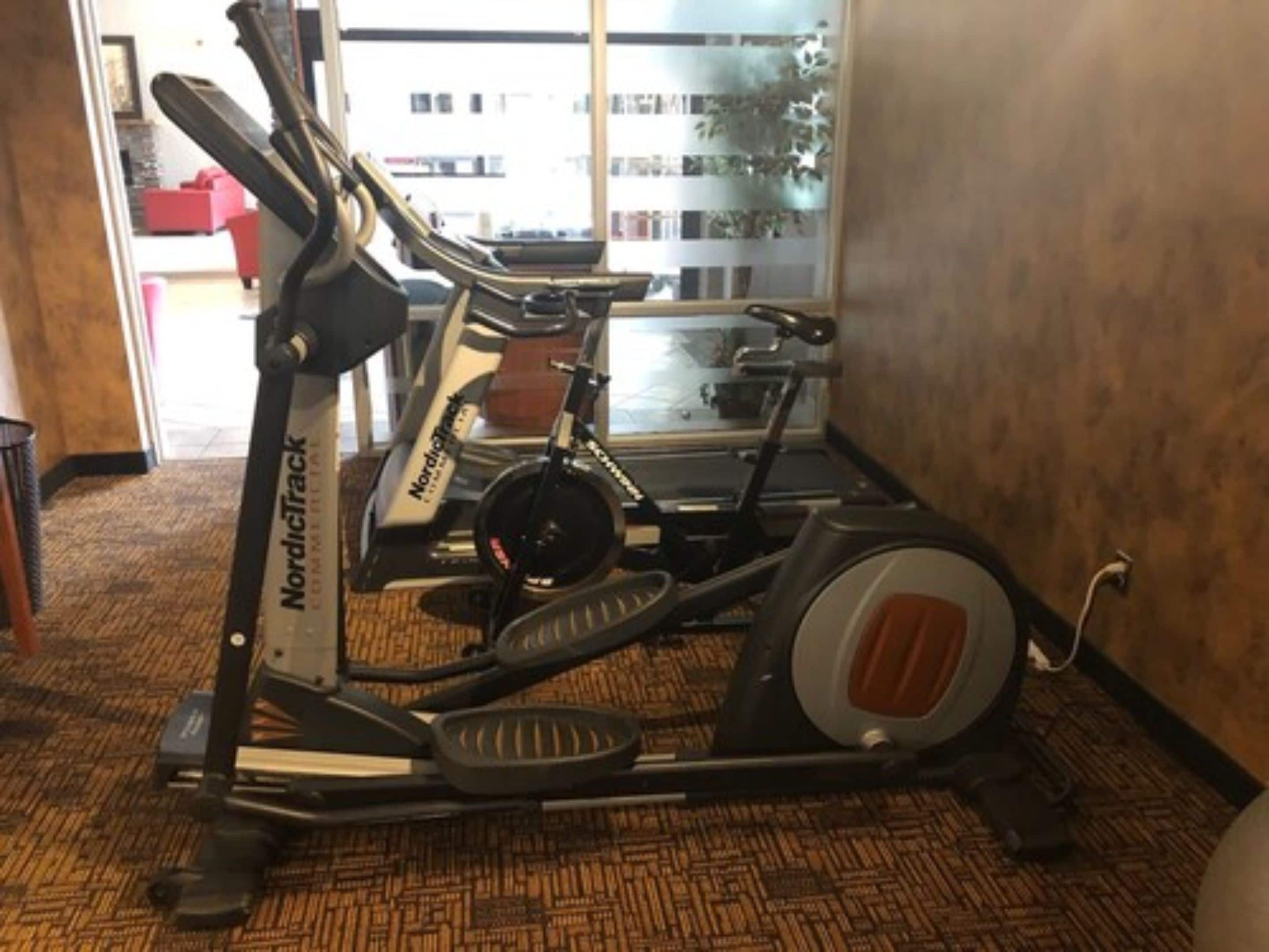 A NordicTrack elliptical machine in a room with patterned carpet, a window with a view of buildings, and a door leading outside.