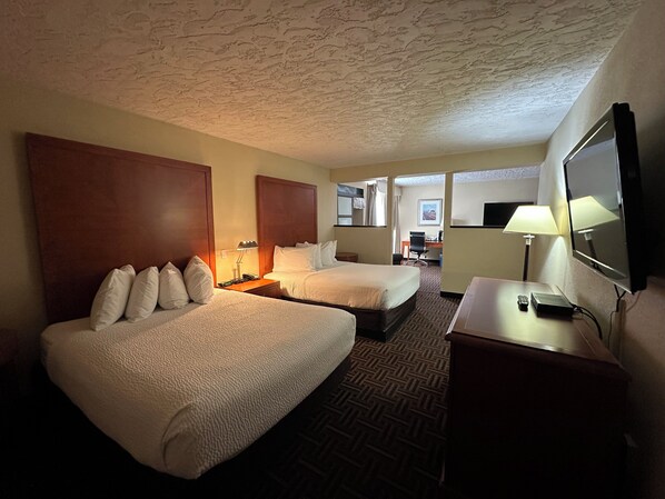 A hotel room with two beds, a desk, a chair, a lamp, and a television.