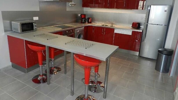 Une cuisine moderne avec des meubles de rangement rouges, des appareils électroménagers en acier inoxydable et un îlot central doté de tabourets.