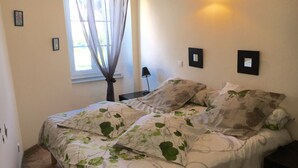 Une chambre à coucher avec un lit, une table de chevet, une lampe et une fenêtre avec des rideaux.