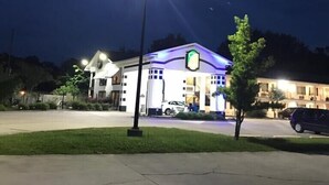 Un hotel bien iluminado con un llamativo letrero verde y blanco, un estacionamiento y una farola.
