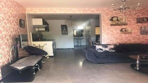 Ein Wohnzimmer mit einer Couch, einem Esstisch und einer Küchenzeile im Hintergrund.