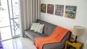 Una sala de estar moderna con un sofá gris, una manta naranja y una pequeña mesita de madera con una lámpara. Cuatro obras de arte decoran la pared sobre el sofá.