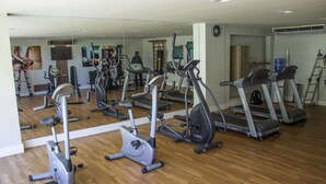 Un gimnasio con diferentes máquinas de cardio, un espejo y suelo de madera.