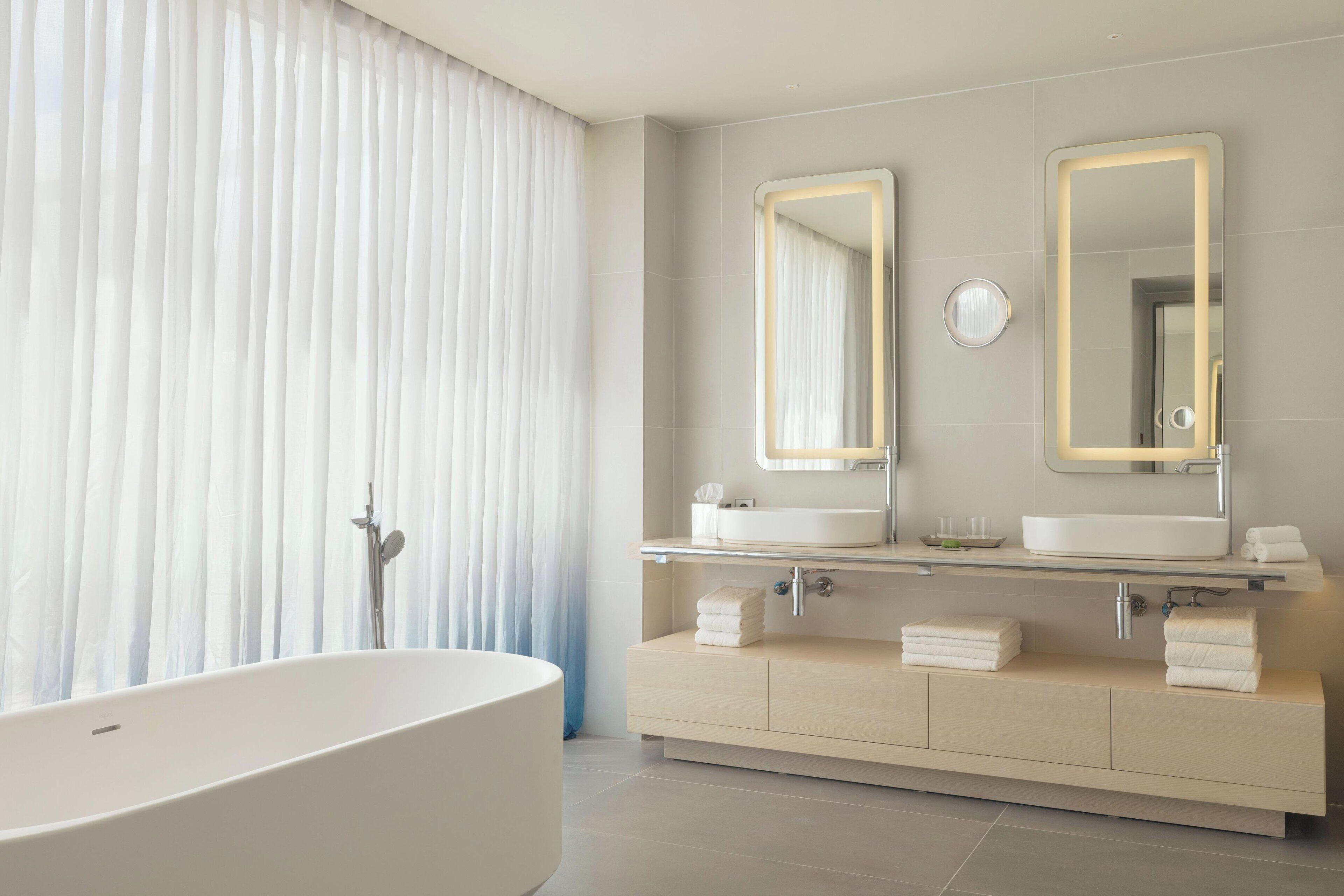 Een moderne badkamer met een vrijstaand bad, twee wastafels en een wastafelmeubel met een spiegel.