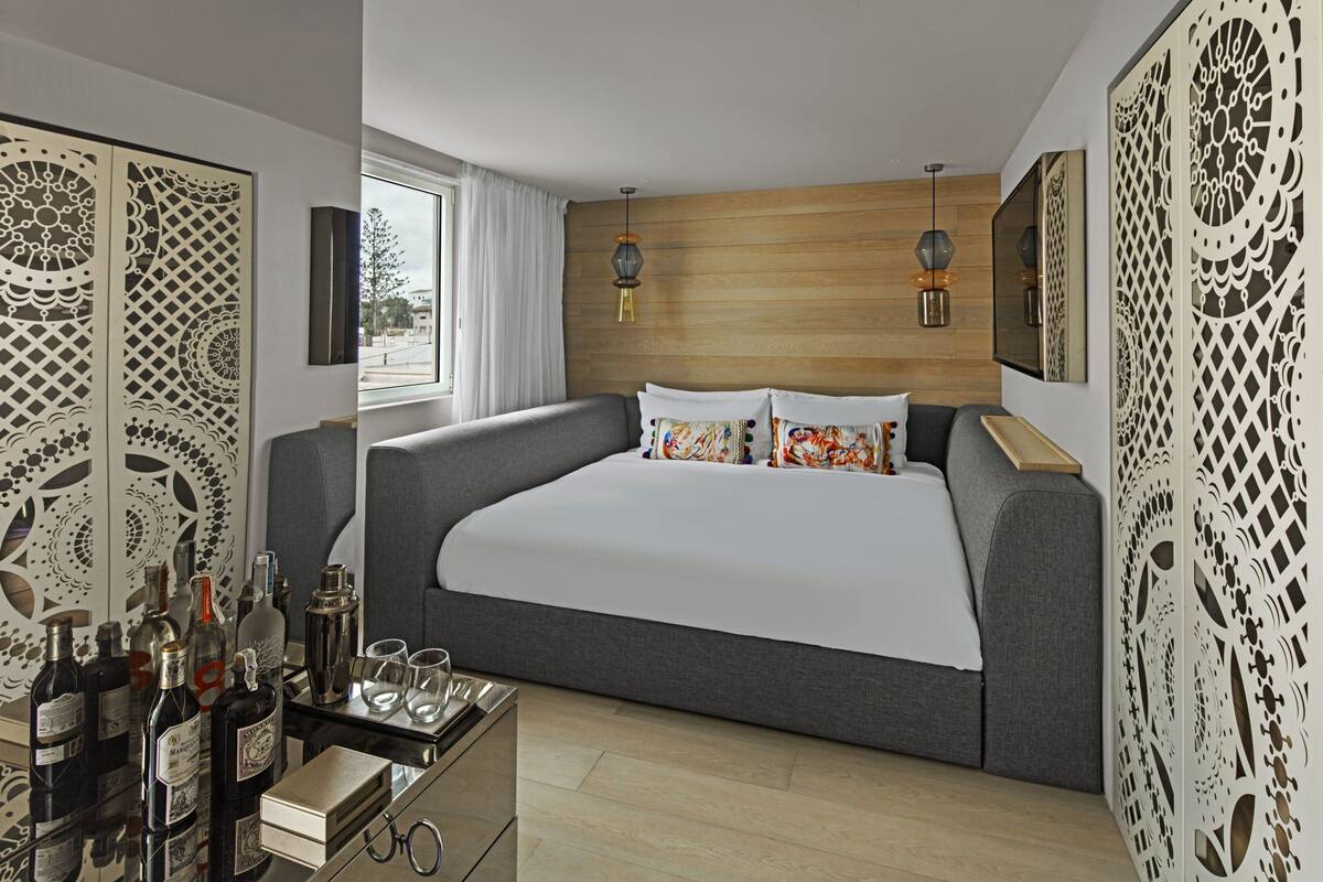 Un dormitorio moderno con una cama grande, cabecera de madera, paneles decorativos, una mesita de noche con botellas, vasos y una bandeja.