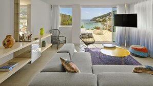 Uma sala de estar moderna com sofá, cadeiras, televisão e varanda com vista para o mar.