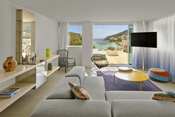 A modern living room with a sofa, chairs, a TV, and a balcony with a view of the sea. - W Ibiza (Santa Eulalia del Rio)