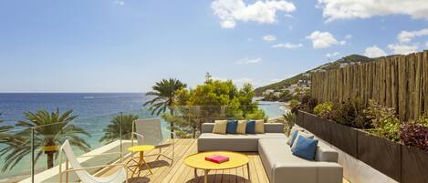 A wooden deck with a sofa, chairs, and a table overlooking the sea.