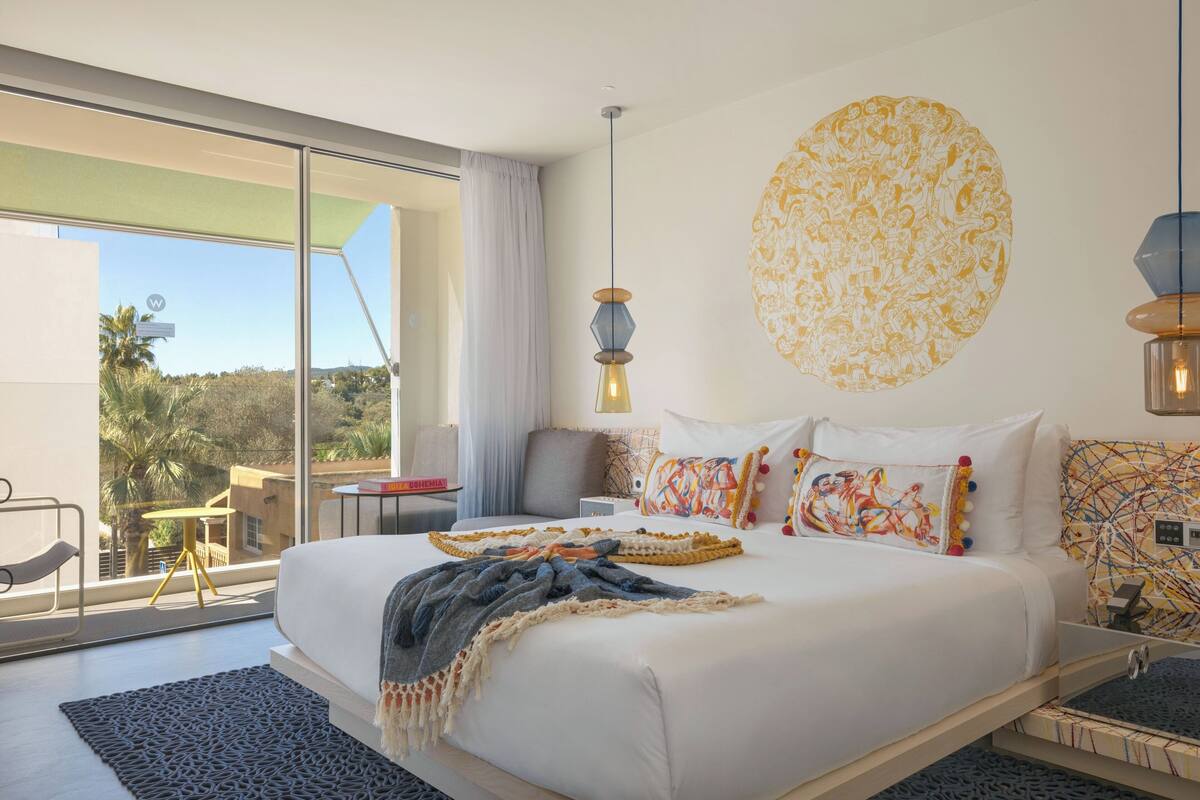 Una habitación de hotel moderna con una cama grande, vistas al exterior y una pieza de arte original en la pared.