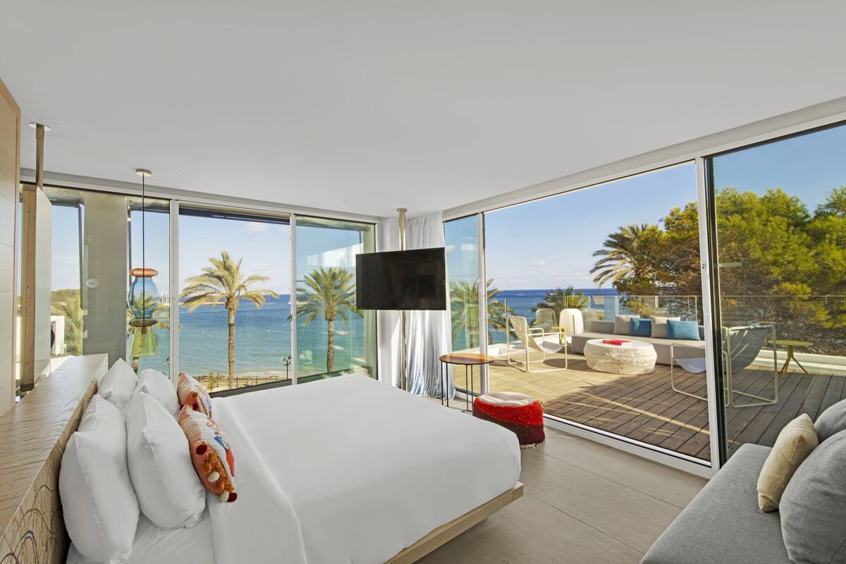 Una habitación de hotel moderna con una cama grande, televisión y balcón con vista al mar.