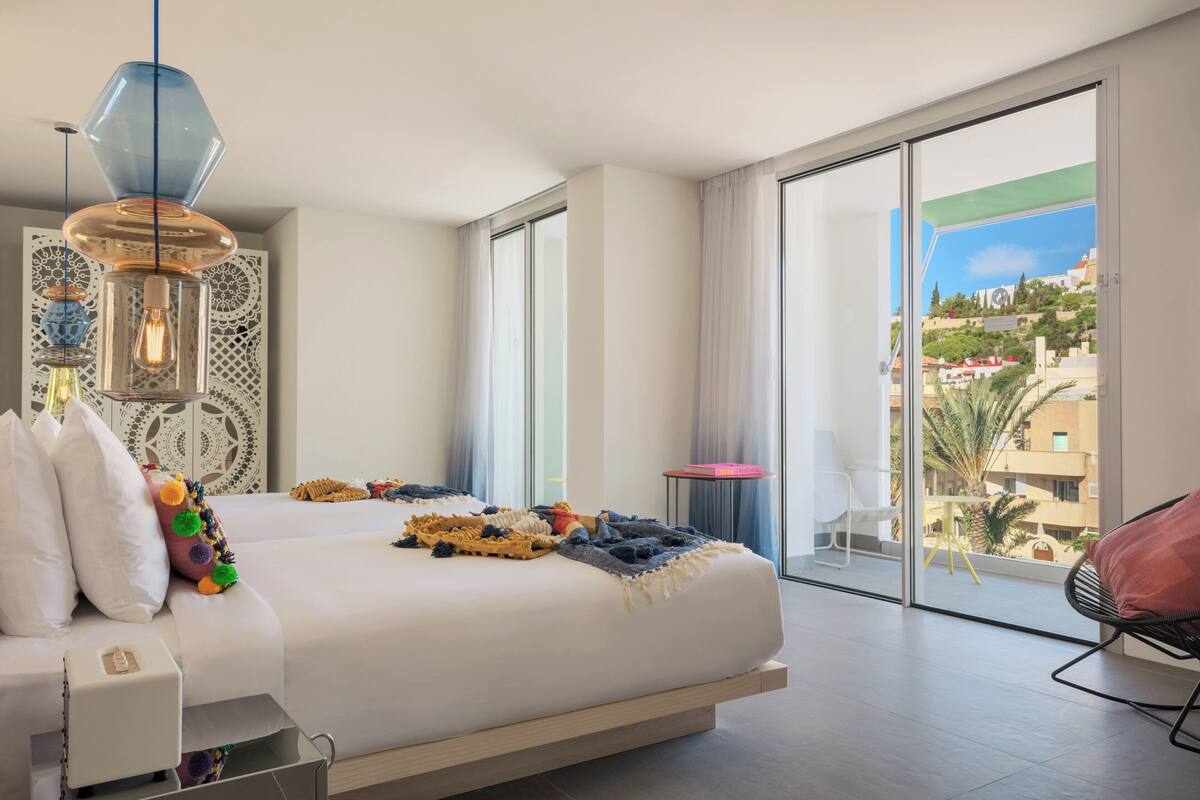 Una habitación de hotel moderna con una cama grande, un balcón con vistas y una pequeña mesa con una silla.