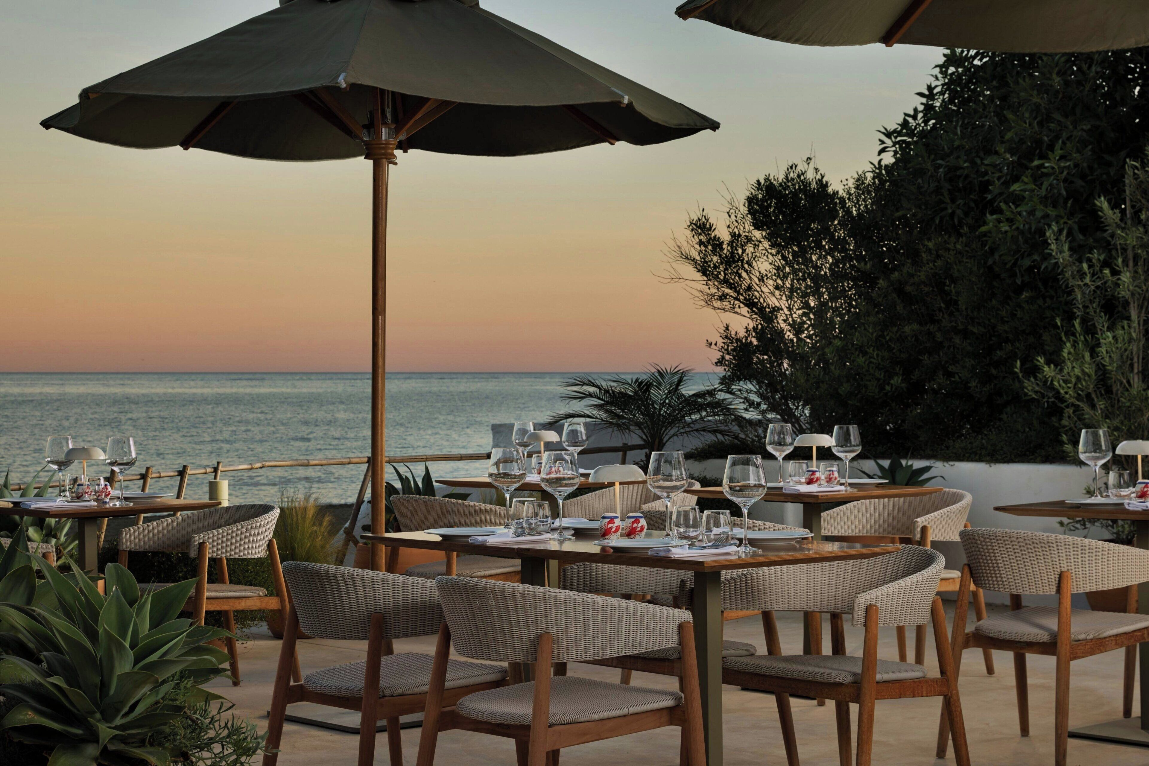 Un espace extérieur aménagé pour les repas, avec des tables, des chaises et des parasols, offrant une vue sur la mer.