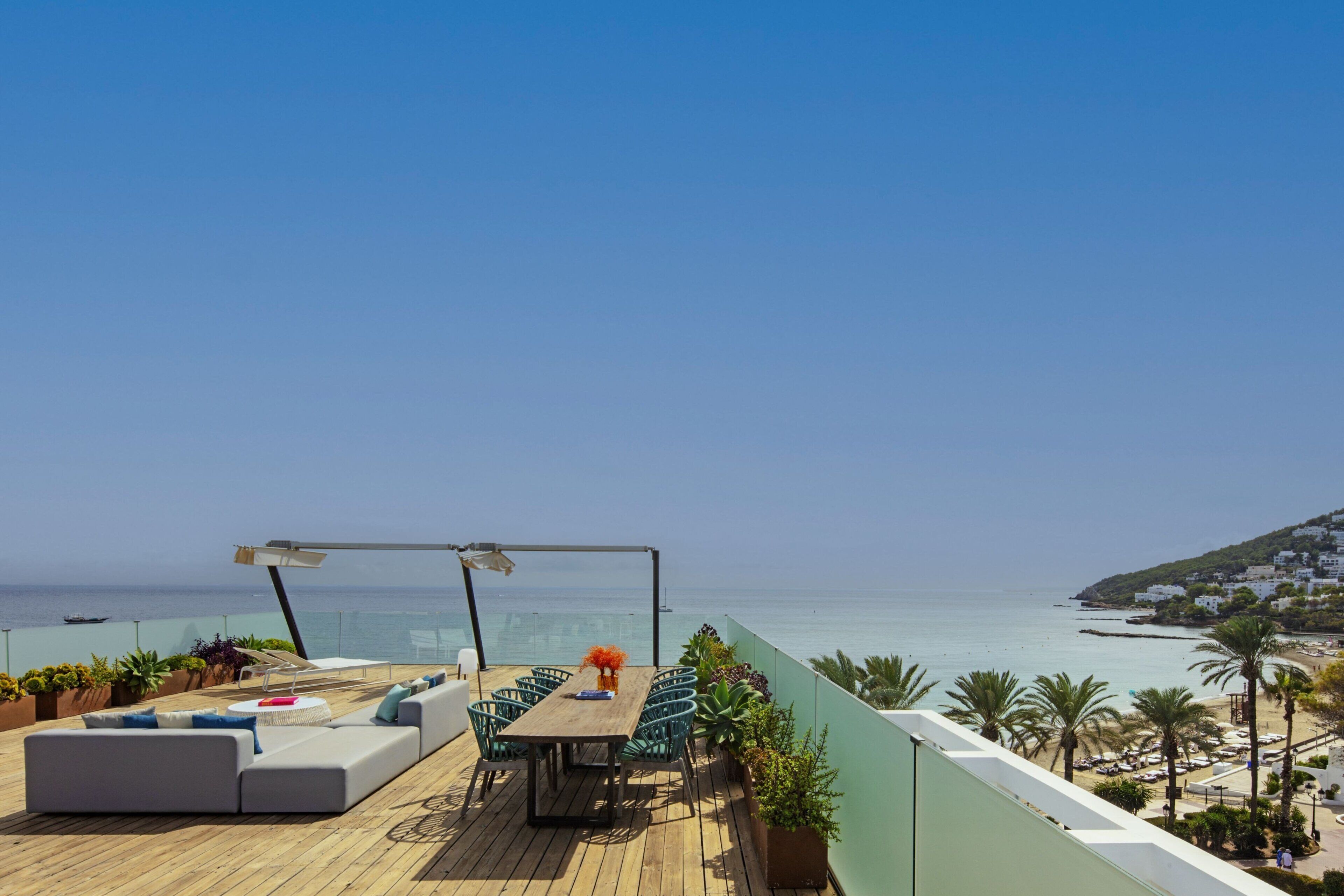 A wooden deck with a table and chairs, overlooking a beach and ocean.